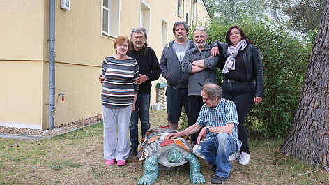 Gruppe vor Haus mit Schildkrötenskulptur