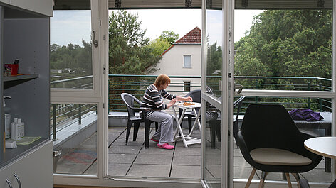 Person sitzt am Tisch auf dem Balkon