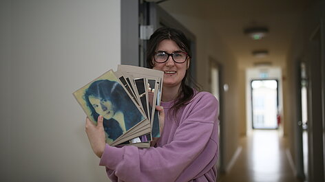 Frau hält Stapel Kunstbilder im Flur