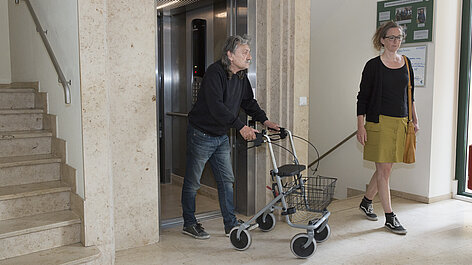 Mann mit Rollator fährt aus dem Aufzug