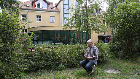Mann schreibt im Garten vor Gebäude